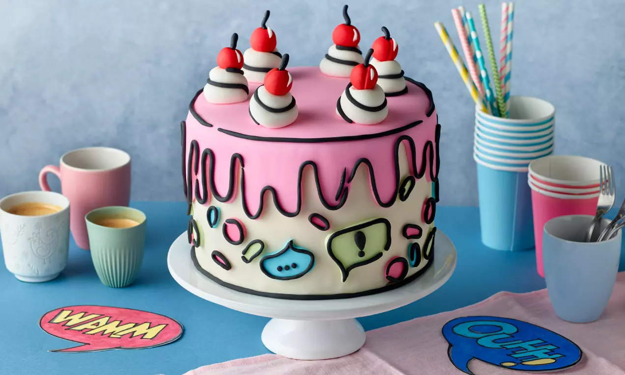 Rosa Torte mit schwarzem Comic-Dekor, weißen Sahnehauben und roten Kirschen auf Tortenplatte, umgeben von bunten Tassen und Comic-Details