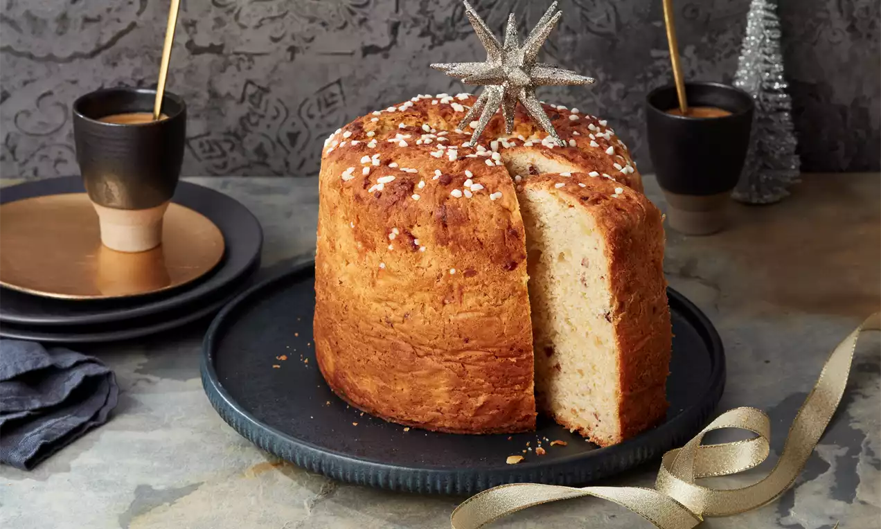 Goldbrauner Panettone mit lockerer Struktur, bestreut mit Zuckerperlen, angeschnitten auf dunkler Platte, dekoriert mit silbernem Stern