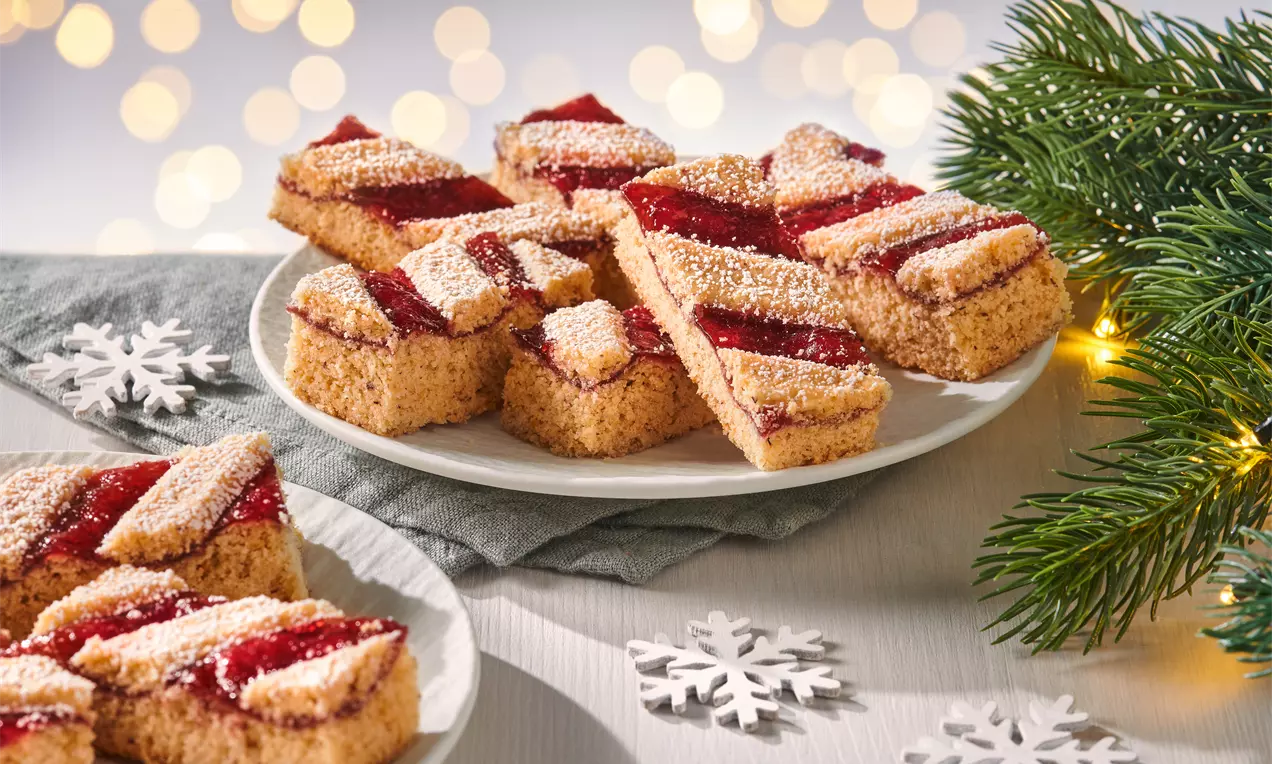 Linzer Streifen mit goldbraunem Mürbeteig und fruchtig roter Füllung, diagonal arrangiert und mit Puderzucker bestäubt auf weißen Tellern