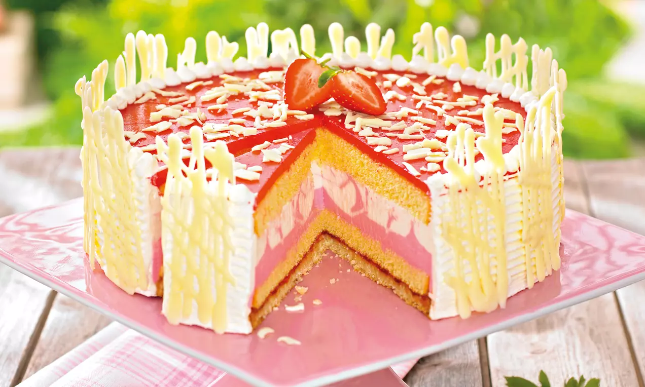 Holler-Torte mit Schichten aus goldgelbem Biskuit, rosa Cremes und rotem Gelee, dekoriert mit weißer Schokolade und Erdbeeren auf rosa Platte