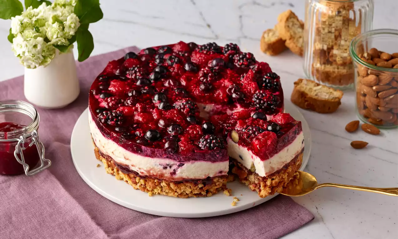 Kleine Beeren-Mandel-Torte mit knusprigem Boden, cremiger Füllung und glänzender Schicht aus schwarzen und roten Beeren auf weißem Teller