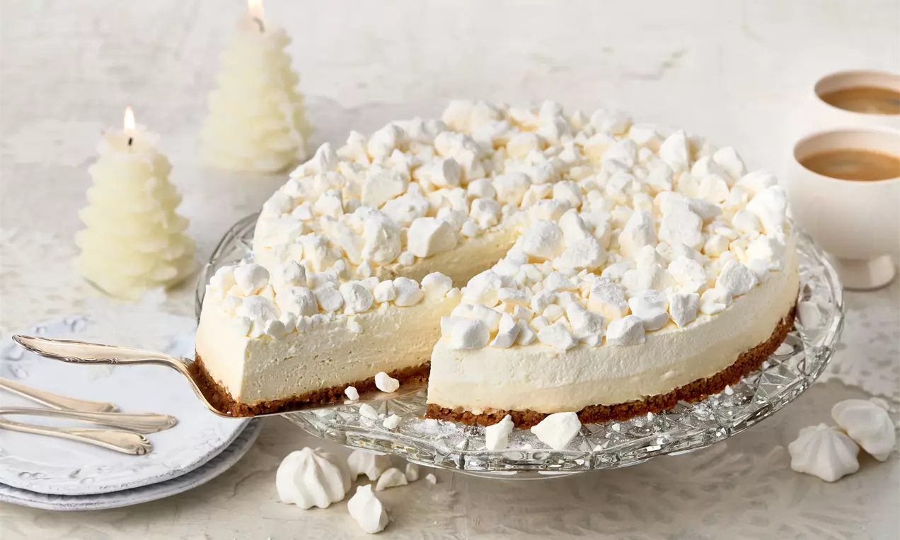 Schneeflöckchen-Torte mit weißer cremiger Füllung auf braunem Boden, bedeckt mit luftigen Baiserstücken auf einer Glasplatte angerichtet