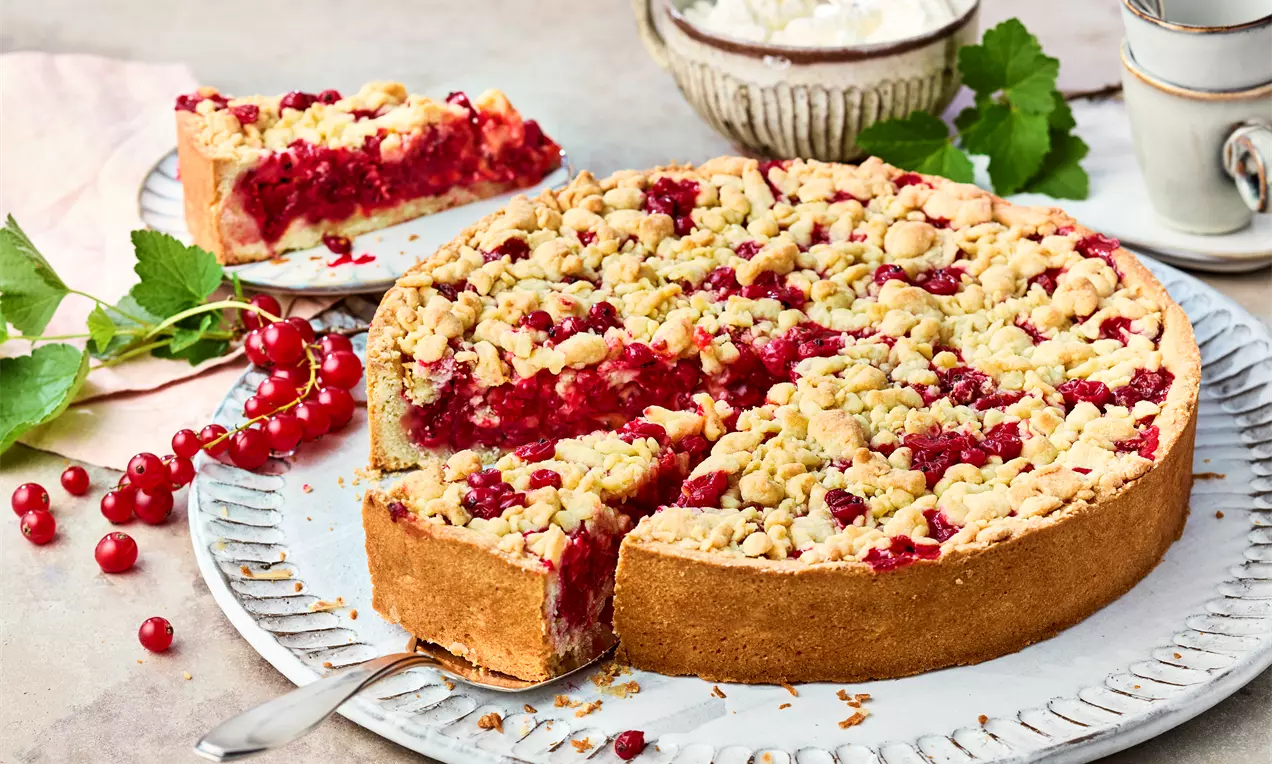 Runder Johannisbeer-Streuselkuchen mit goldbrauner Kruste, saftiger roter Füllung und knusprigen Streuseln auf einem weißen Teller angerichtet