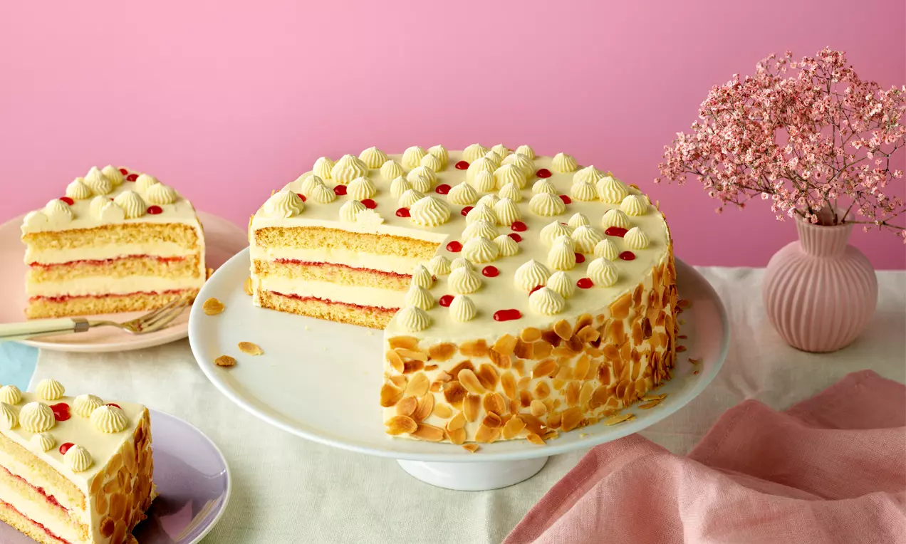 Buttercreme-Torte mit gelber Creme, Schichten aus heller Füllung und rosa Gelee, gerösteten Mandelblättchen und Sahnetupfen auf Tortenplatte