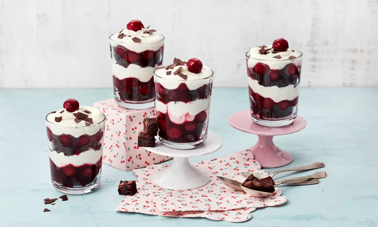 Schwarzwälder-Kirsch-Dessert im Glas mit abwechselnden Schichten aus weißer Sahnecreme und dunkler Kirschfüllung, dekoriert mit Schokoraspeln und Kirschen