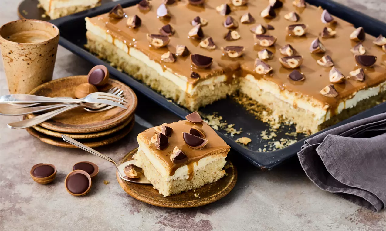 Rechteckiger Kuchen mit hellgelber Creme und karamellfarbener Glasur, belegt mit halbierten Toffifees, auf Blech und Tellern angerichtet