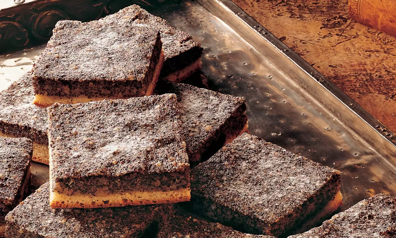 Blechkuchen aus goldgelbem Grießboden und dunkler, saftiger Mohnschicht in rechteckige Stücke geschnitten auf Metallplatte angerichtet