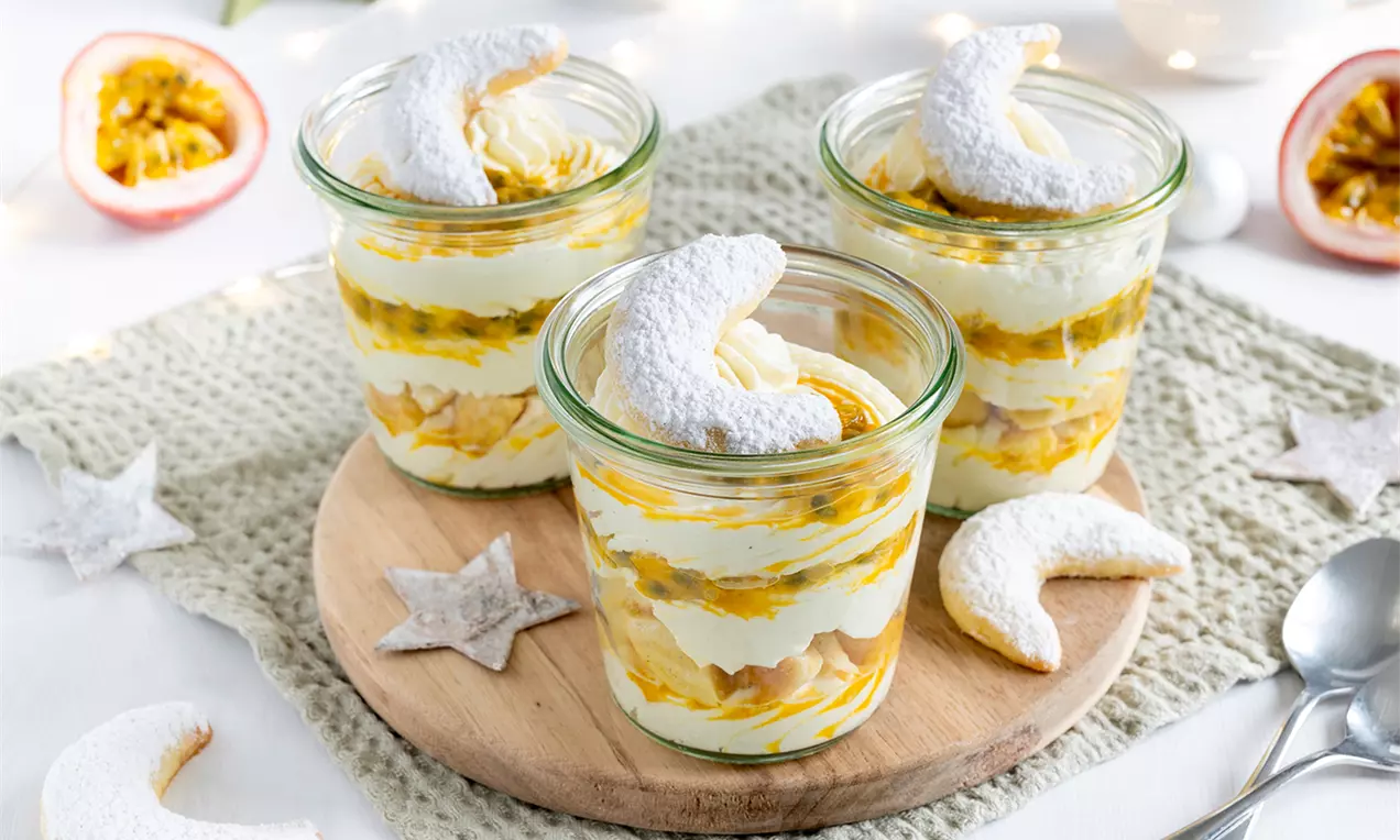 Vanillekipferl-Tiramisu in kleinen Gläsern mit Schichten aus heller Creme, goldgelber Passionsfruchtsauce und bestäubtem Kipferl, dekoriert auf einem Holzbrett