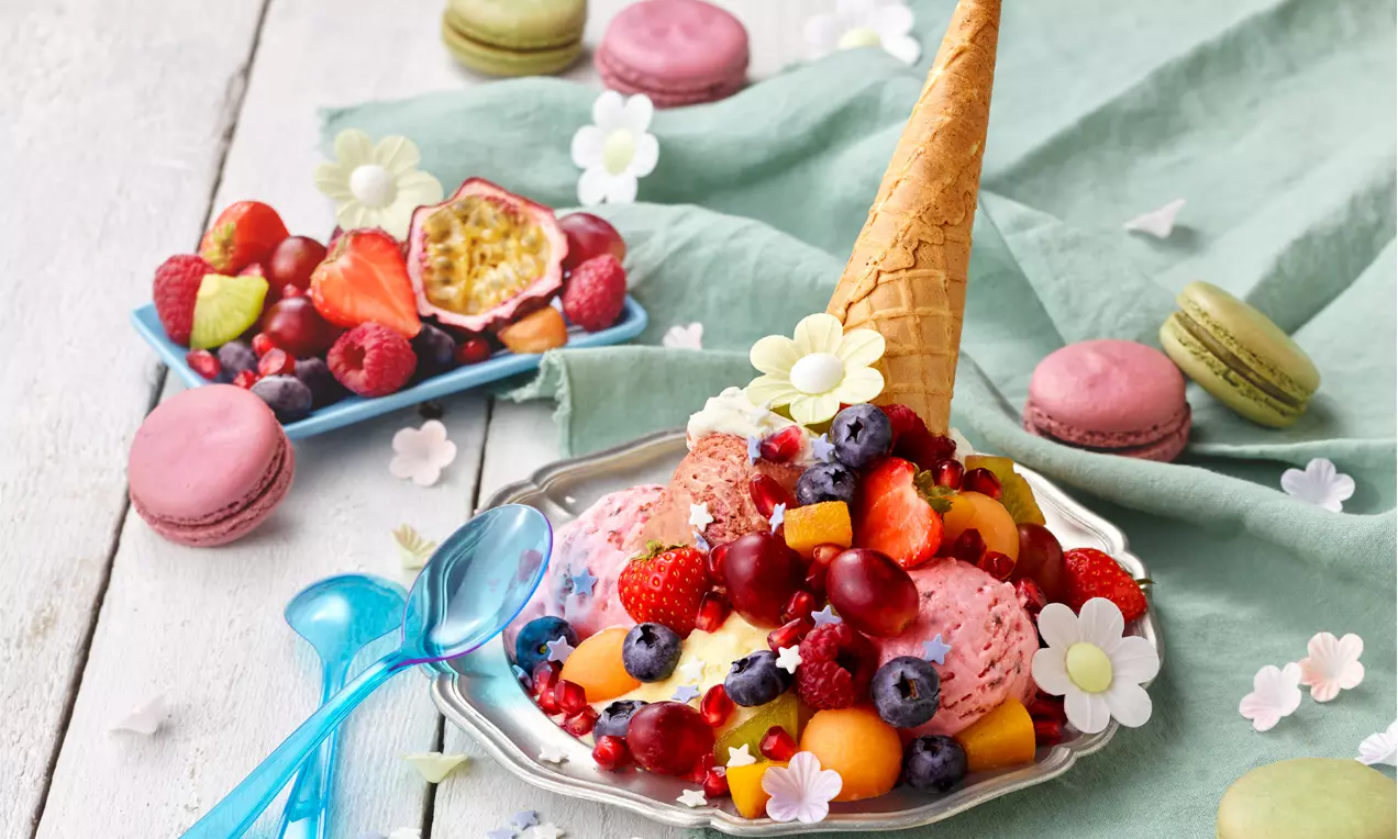 Bunter Eisbecher mit kugelförmigen Portionen, frischen Beeren, Melonenstücken, Waffeltüte, Zuckerblüten, Serviert auf silbernem Teller