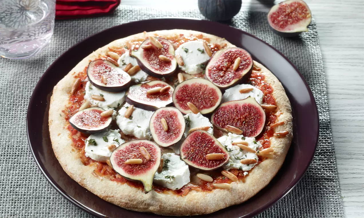 Runde Pizza mit goldbraunem Rand, belegt mit Ziegenkäse, frischen Feigen und Pinienkernen, auf einem dunkelbraunen Teller angerichtet