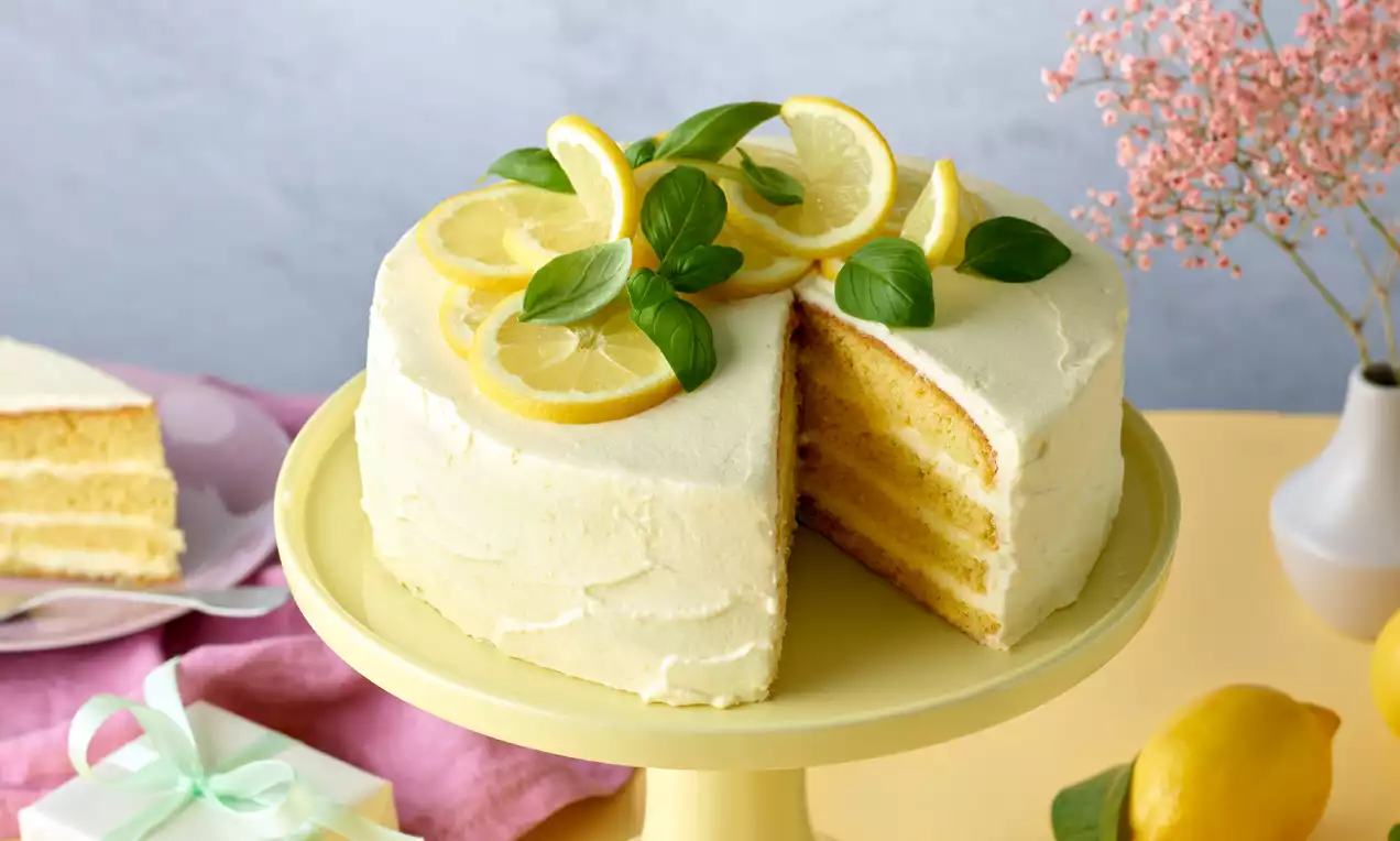 Helle Torte aus Biskuitböden und Zitronencreme mit Zitronenscheiben dekoriert.