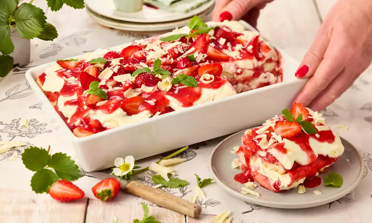 Erdbeer-Lasagne mit Schichten aus Sahnecreme, frischen Erdbeeren und Keksen in einer weißen Form, serviert auf einem dekorierten Tisch