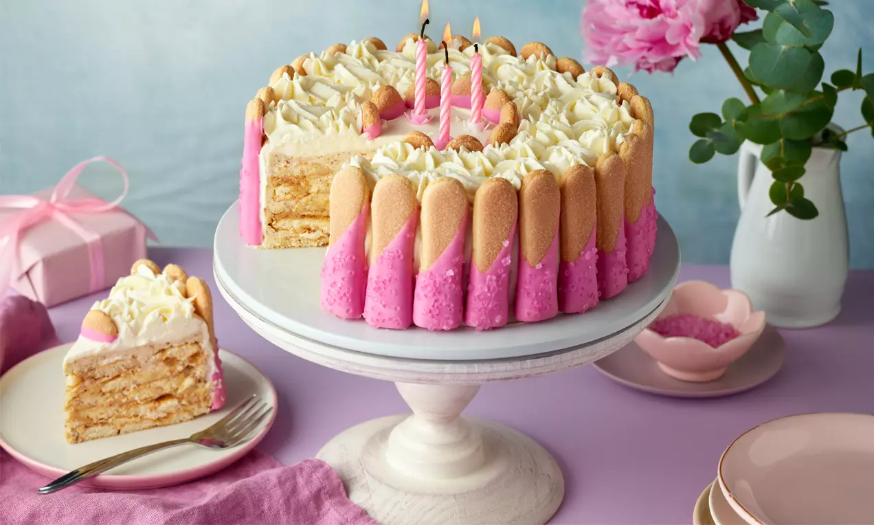 Runde Malakoff-Torte mit hellen Biskuits und rosa Creme am Rand, Sahnetuffs und rosa Kerzen auf der Oberfläche, auf einer weißen Tortenplatte