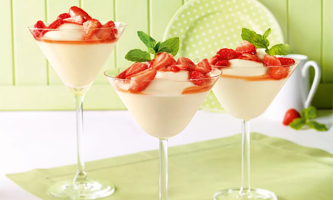 Cremiger Holunderblüten-Pudding in eleganten Cocktailgläsern, belegt mit glänzenden roten Erdbeerstückchen und frischen Minzblättern