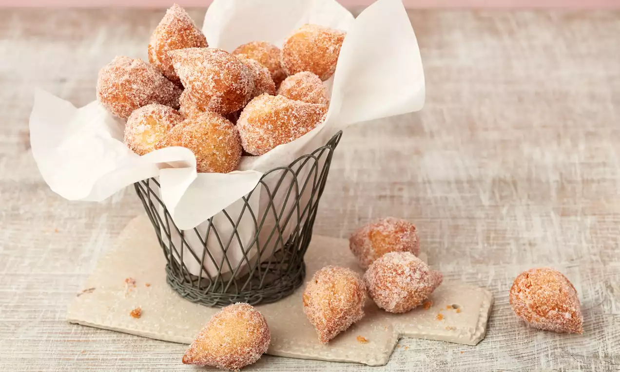 Goldbraune, ungleichmäßige Muzenmandeln mit feinkörnigem Zuckerüberzug in einem Drahtkorb auf hellem Papier dekorativ drapiert