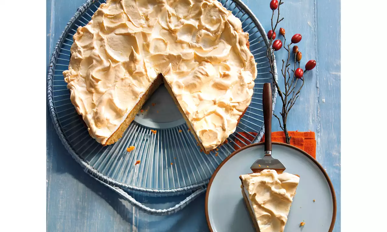Birnenkuchen mit welliger, goldbrauner Baiserhaube auf blauem Glasteller, ein angeschnittenes Stück auf einem Teller mit Tortenheber