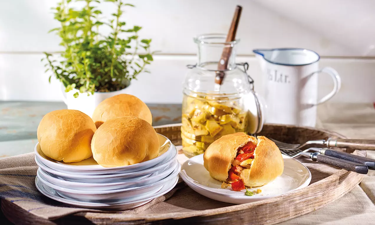 Goldbraune, fluffige Hefekugeln mit glänzendem Antipasti-Gemüse gefüllt, auf weißen Tellern auf einem rustikalen Holztablett angerichtet