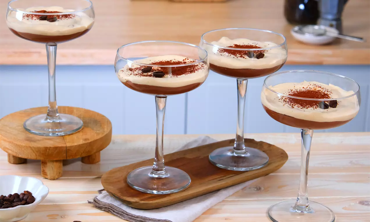 Espresso-Martini-Dessert in eleganten Gläsern, mit samtiger Creme, Espresso-Schicht, Kakao bestäubt und Kaffeebohnen garniert auf Holzbrett arrangiert