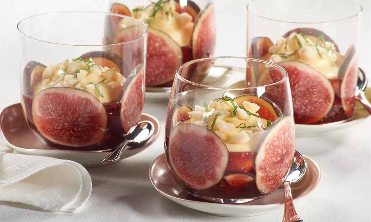 Gläser mit Original-Pudding, umrandet von frischen violett-roten Feigenscheiben, garniert mit hellem Ragout, gehobelten Mandeln und Minzstreifen